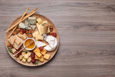 Photo of Cheese plate with honey, grapes and nuts on wooden table, top view. Space for text