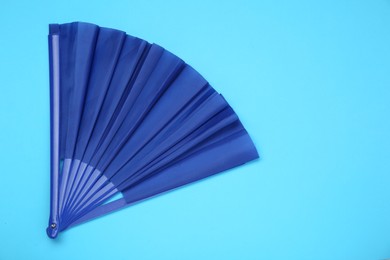 Bright color hand fan on light blue background, top view. Space for text