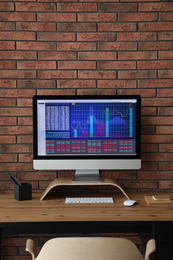 Photo of Modern computer with statistic information on wooden table near brick wall