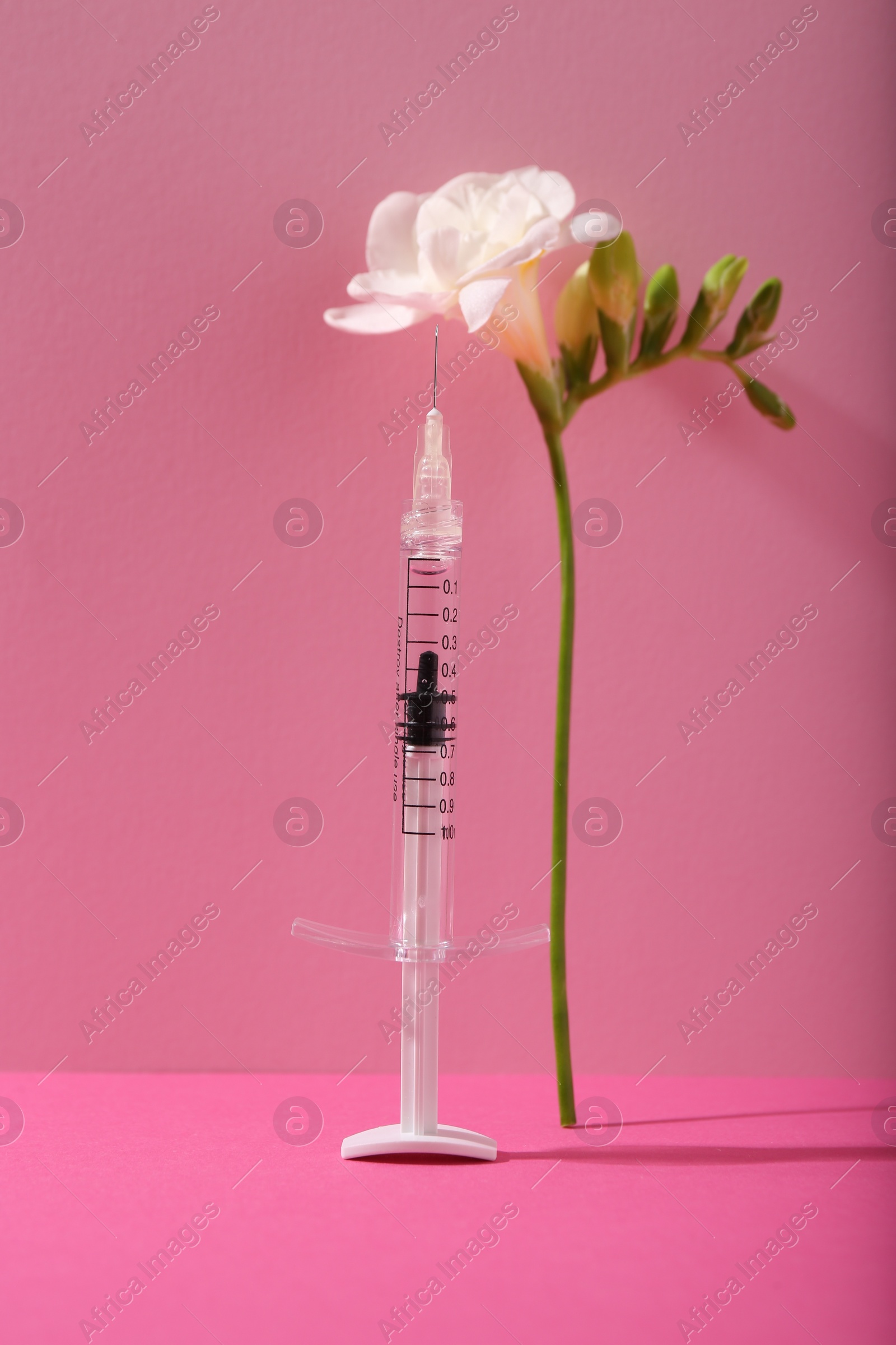 Photo of Cosmetology. Medical syringe and freesia flower on pink background