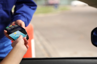 Woman sitting in car and paying with credit card at gas station, closeup