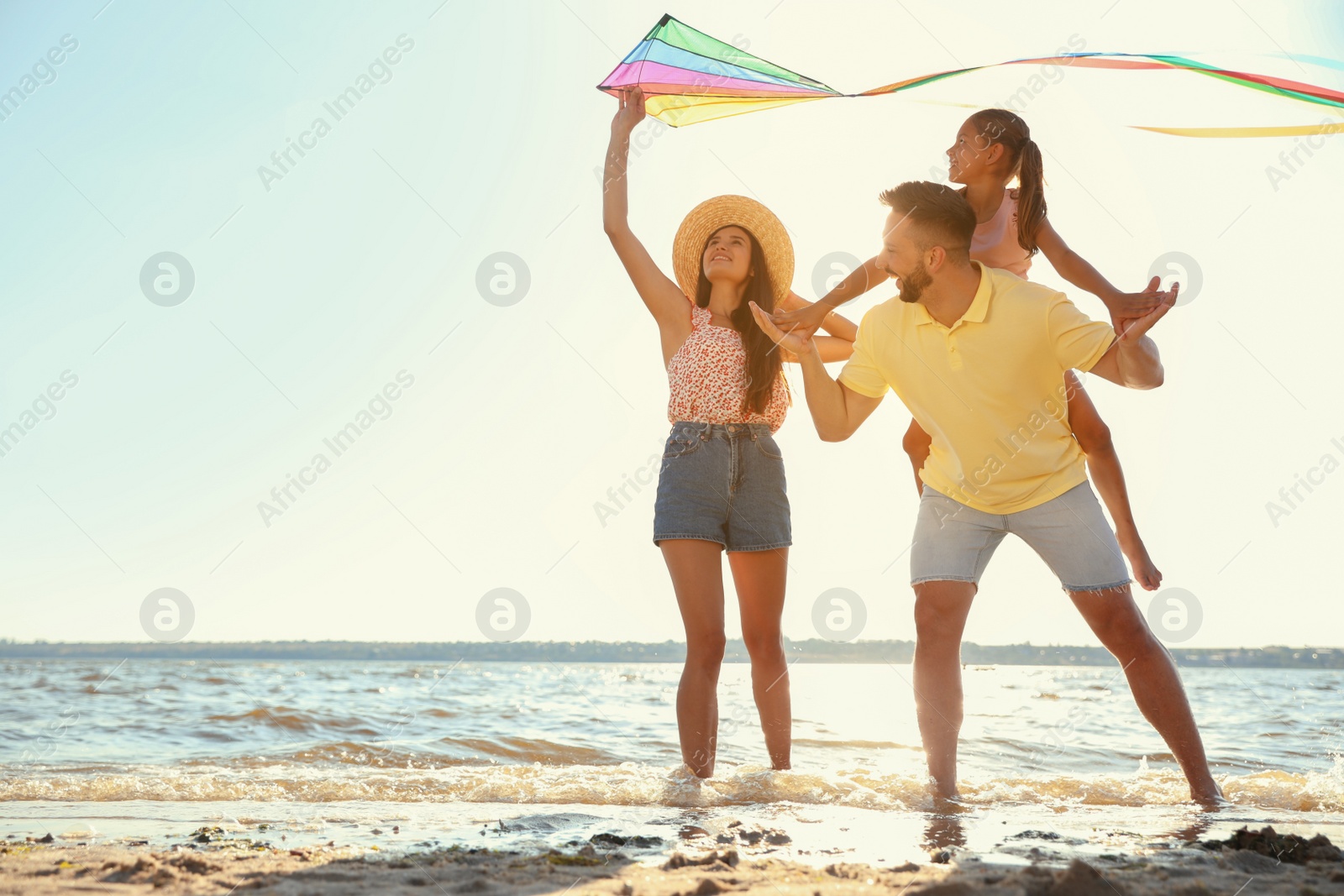 Photo of Happy parents and their child playing with kite on beach near sea. Spending time in nature