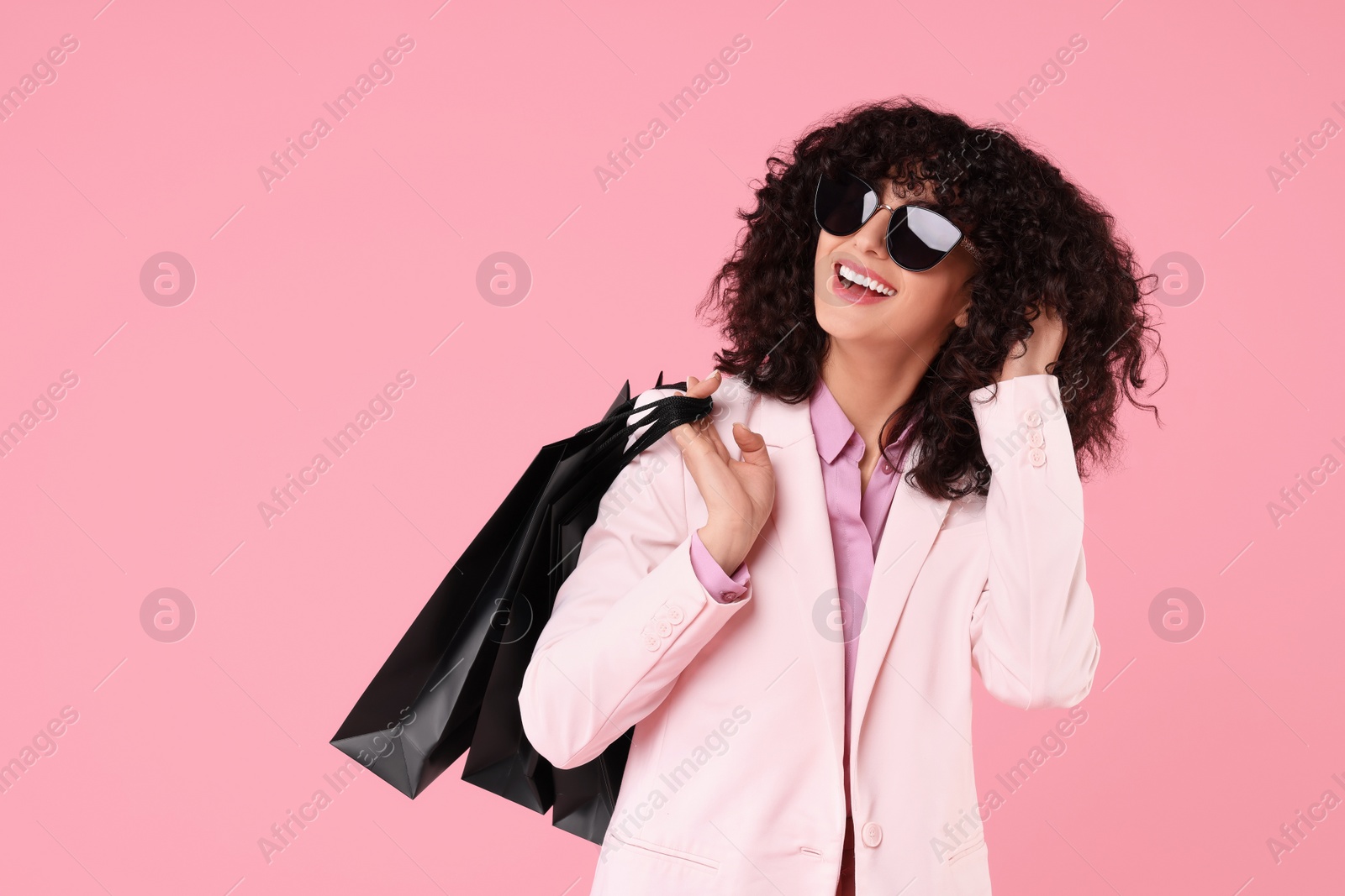 Photo of Happy young woman with shopping bags and stylish sunglasses on pink background
