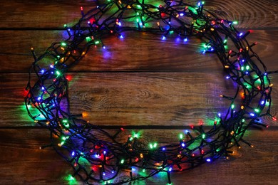 Photo of Glowing festive lights on wooden table, above view. Space for text