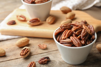 Photo of Tasty pecan nuts in dish served on wooden table. Space for text