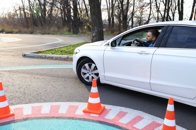 Photo of Young man in car on test track with traffic cones. Driving school