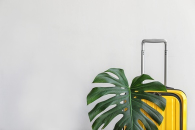 Photo of Bright yellow suitcase with tropical leaf on light background