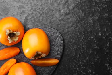 Photo of Delicious ripe persimmons on dark textured table, top view. Space for text