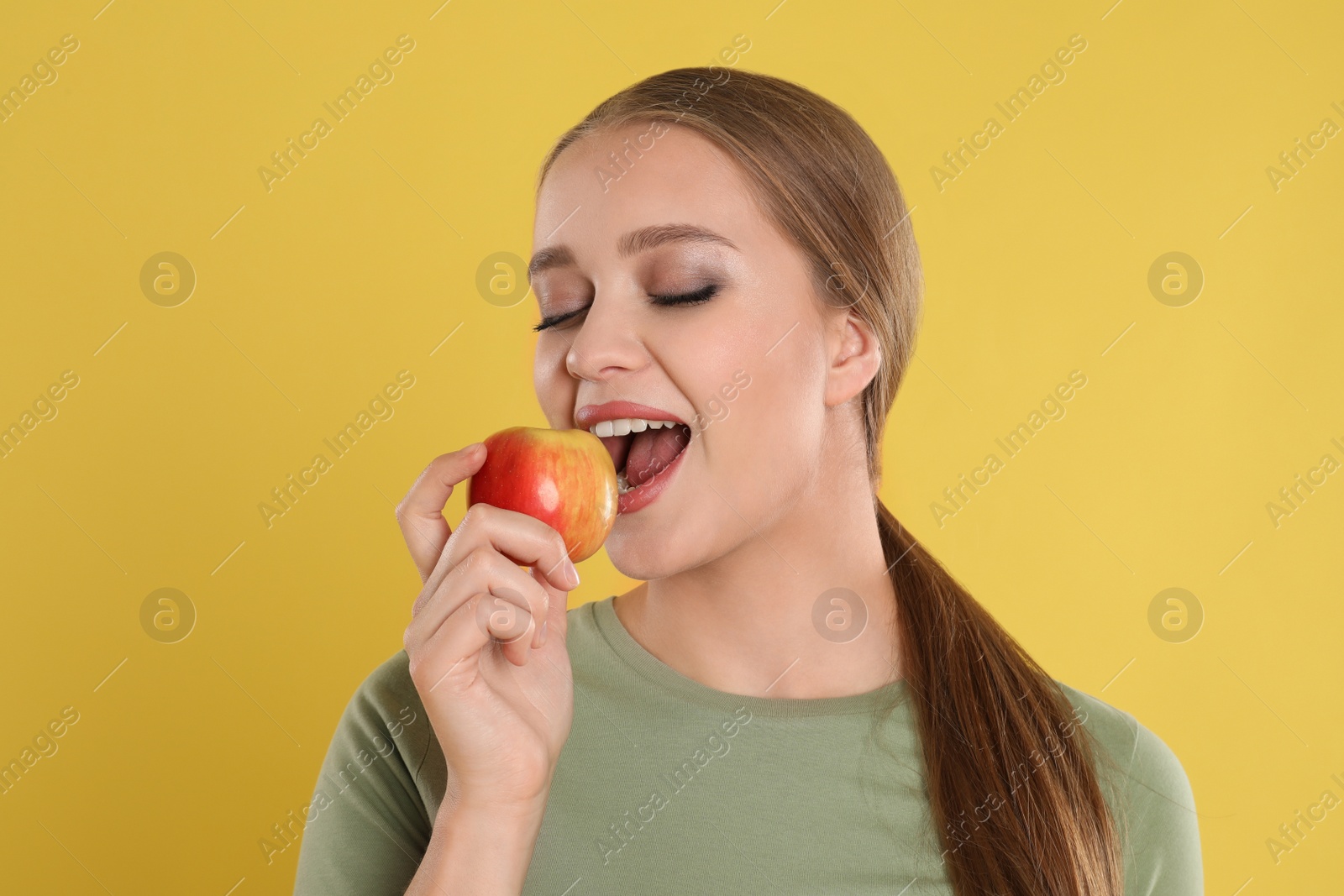 Photo of Young woman with apple on yellow background. Vitamin rich food