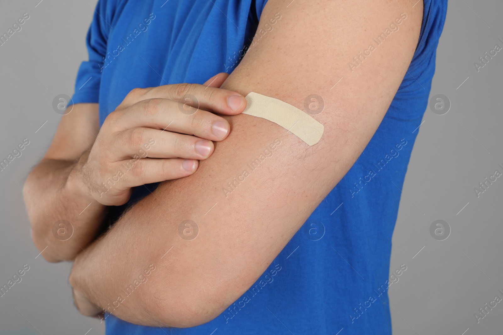 Photo of Vaccinated man with medical plaster on his arm against grey background, closeup