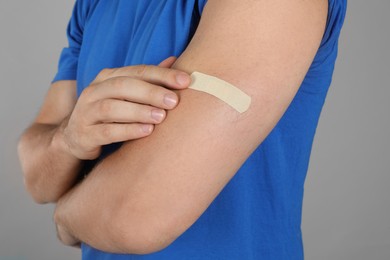 Vaccinated man with medical plaster on his arm against grey background, closeup