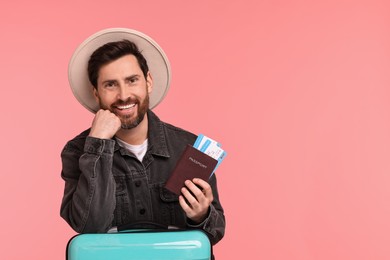 Smiling man with passport, tickets and suitcase on pink background. Space for text
