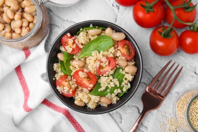 Delicious quinoa salad with tomatoes, beans and spinach leaves served on white textured table, flat lay