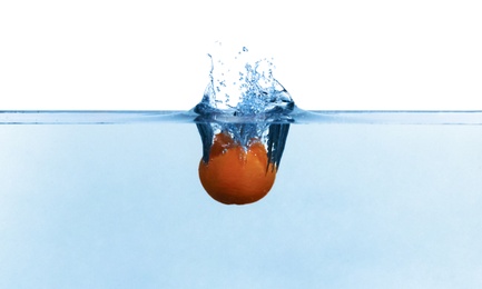 Tangerine falling down into clear water against white background