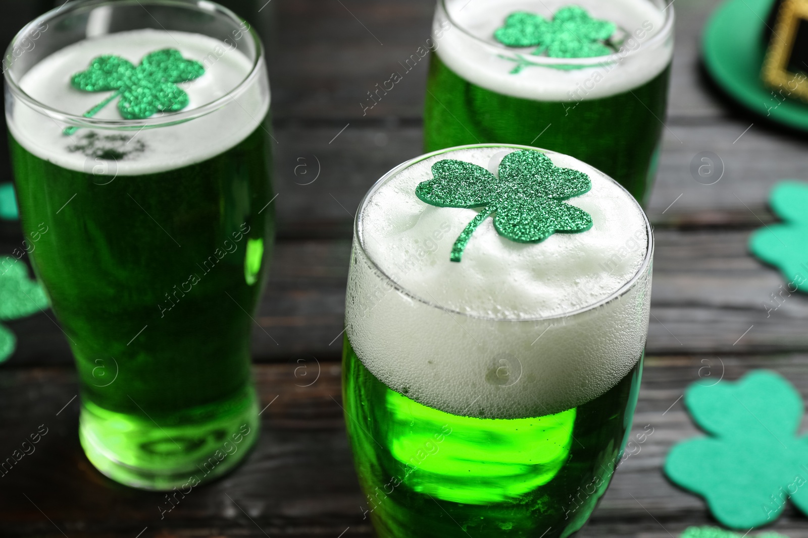 Photo of Green beer and clover leaves on black wooden table, closeup. St. Patrick's Day celebration