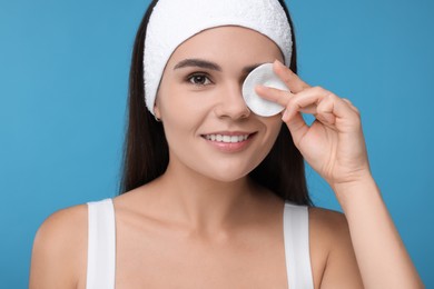 Young woman with cotton pad on light blue background