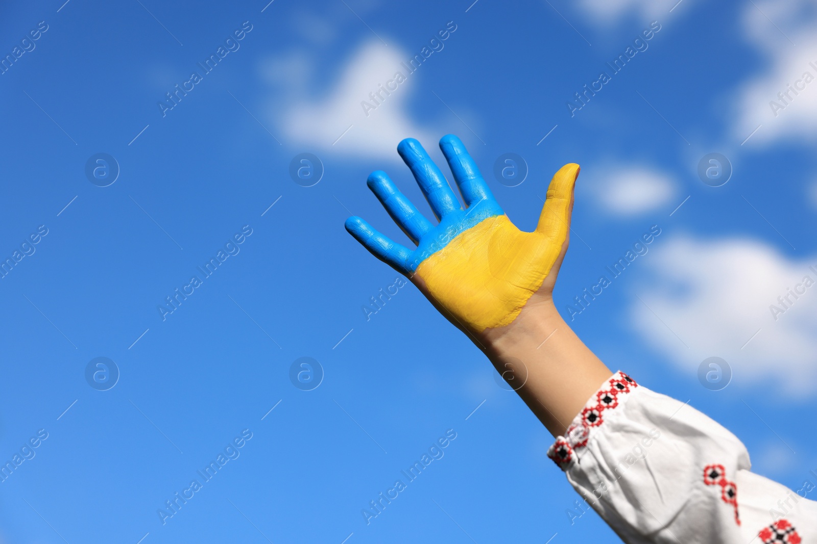 Photo of Little girl with hand painted in Ukrainian flag colors against blue sky, closeup and space for text. Love Ukraine concept