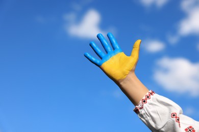 Photo of Little girl with hand painted in Ukrainian flag colors against blue sky, closeup and space for text. Love Ukraine concept