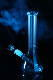 Glass bong and smoke on black background, toned in blue. Smoking device