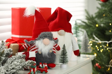 Photo of Funny Christmas gnomes and gift boxes on commode in room with festive decoration