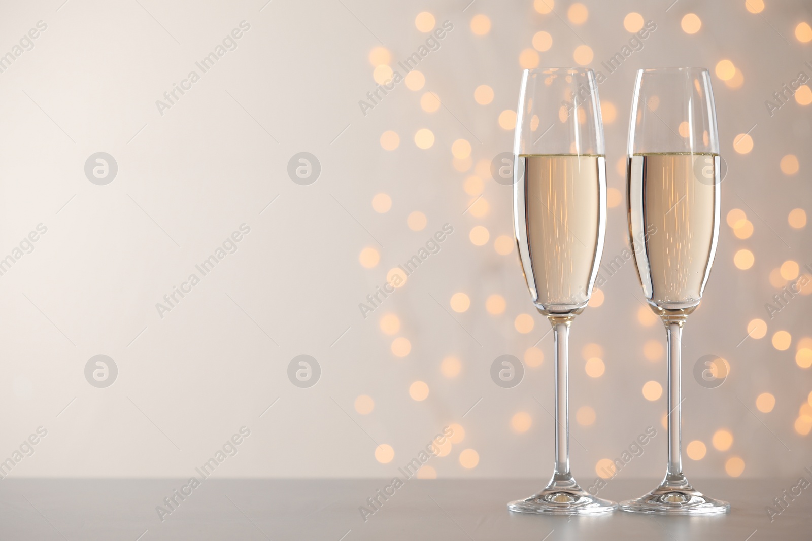 Photo of Glasses of champagne on grey table against blurred lights. Space for text