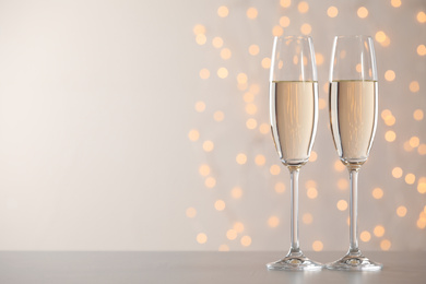 Photo of Glasses of champagne on grey table against blurred lights. Space for text