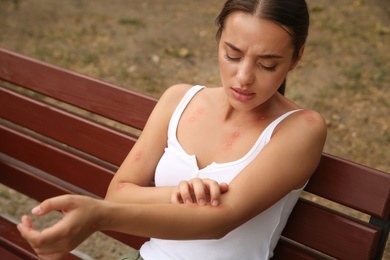 Photo of Woman scratching arm with insect bite outdoors
