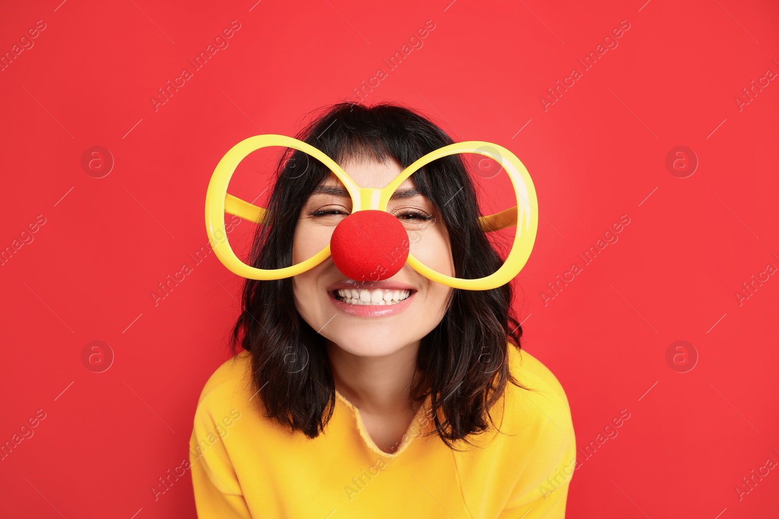 Photo of Joyful woman with large glasses and clown nose on red background. April fool's day