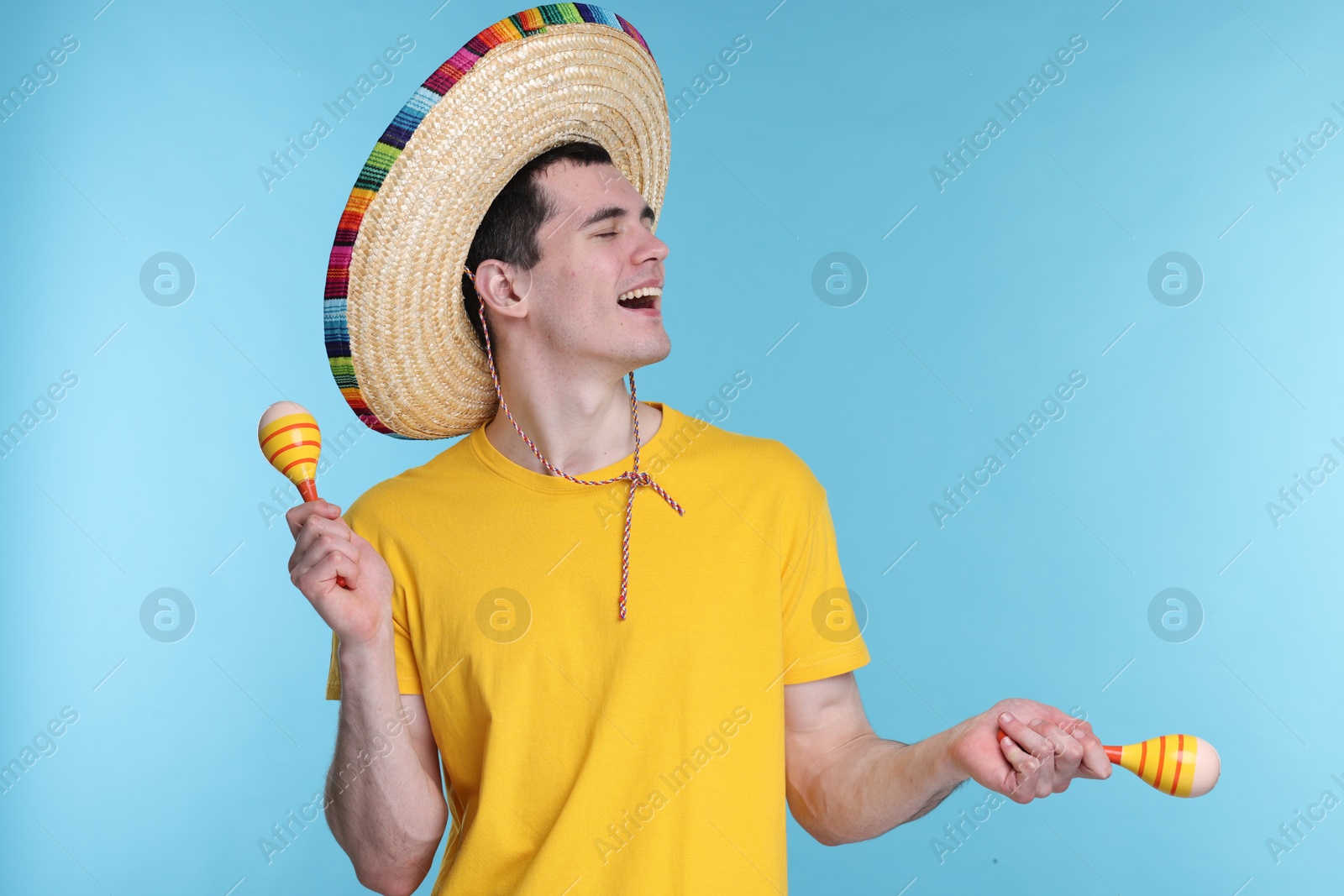 Photo of Young man in Mexican sombrero hat with maracas on light blue background