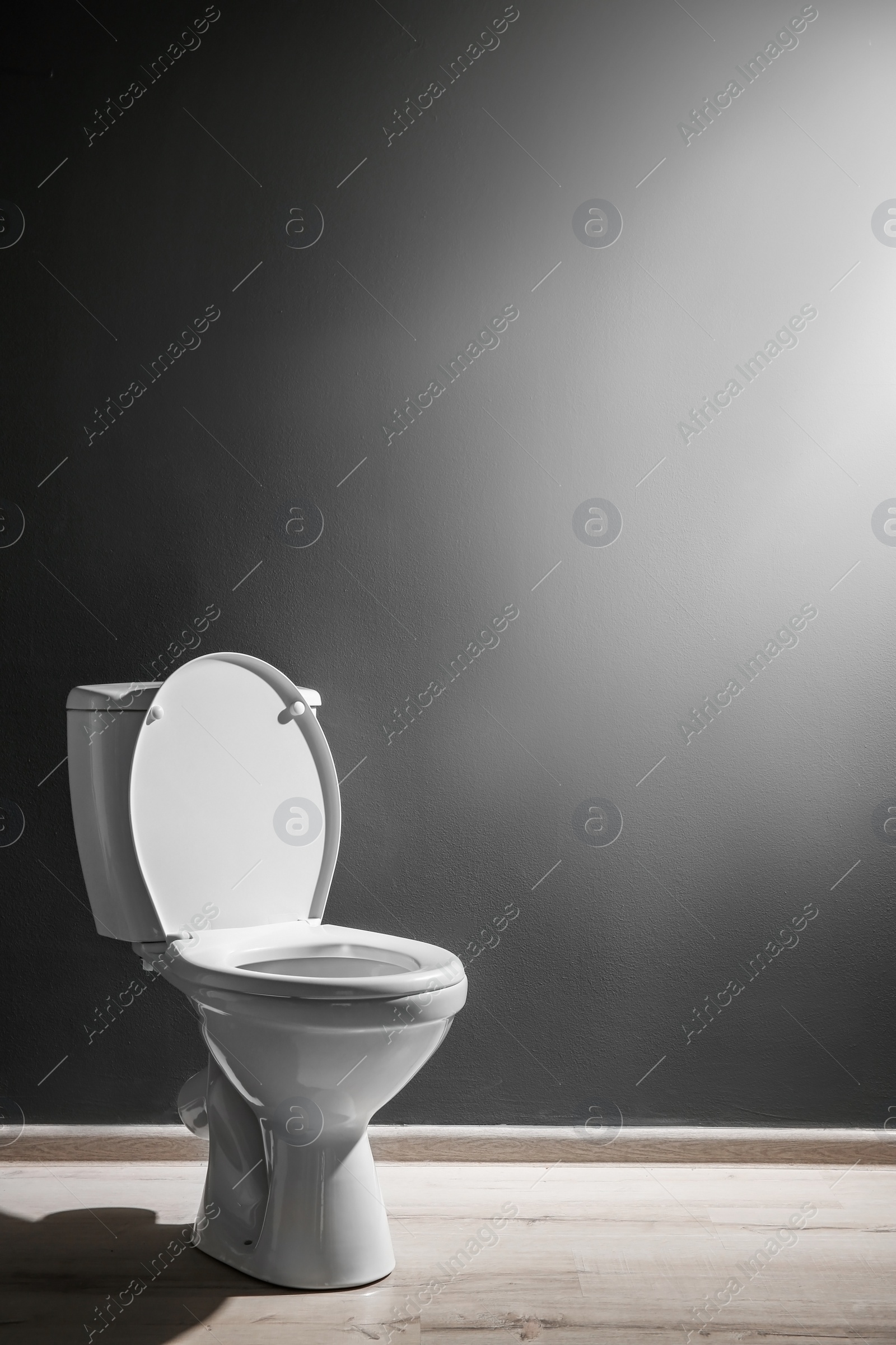 Photo of New ceramic toilet bowl near grey wall, side light