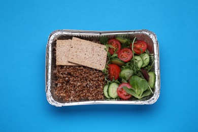 Container with buckwheat, fresh salad and crispbreads on light blue background, top view