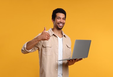 Happy man with laptop showing thumb up on orange background