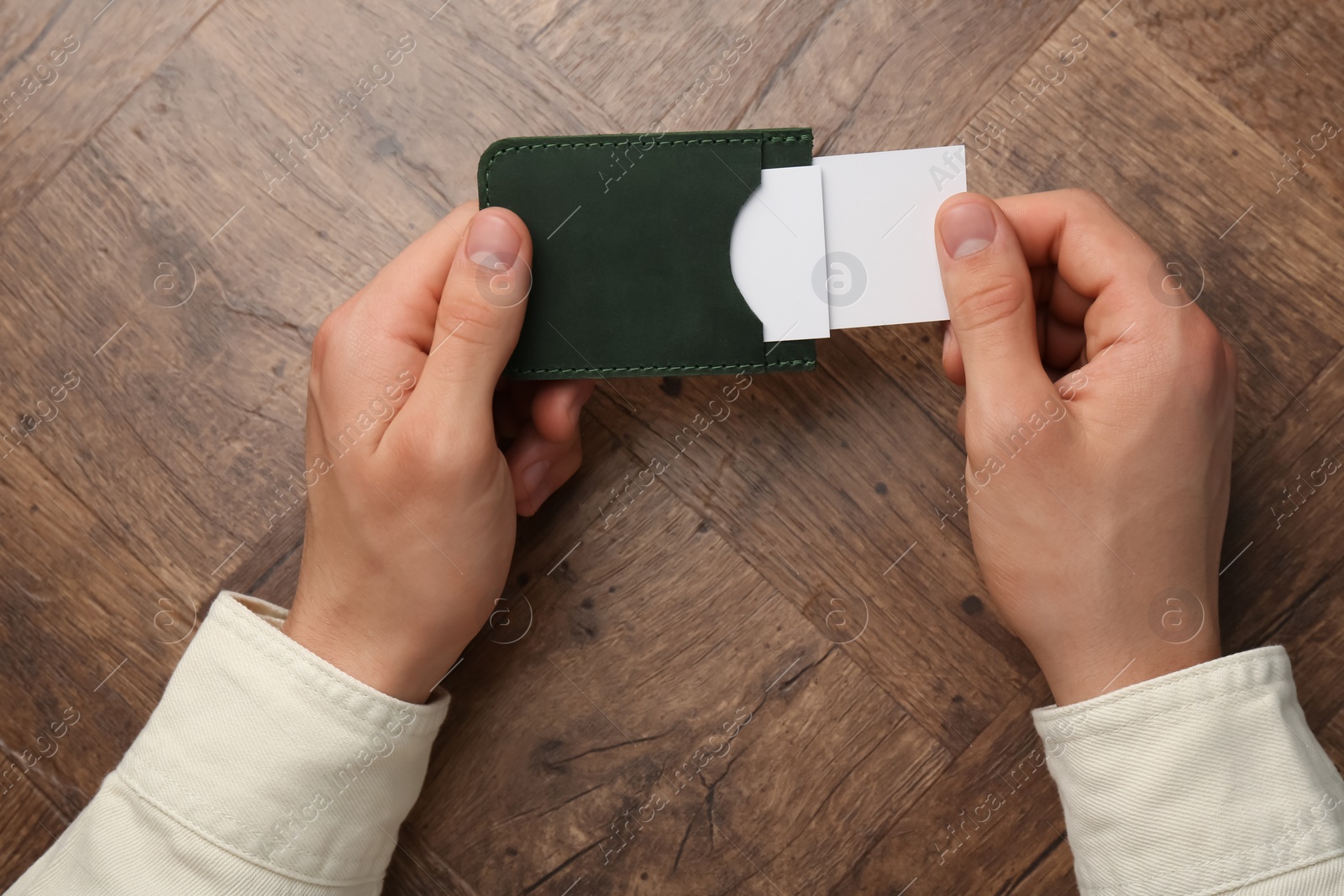 Photo of Man holding leather business card holder with cards at wooden table, top view