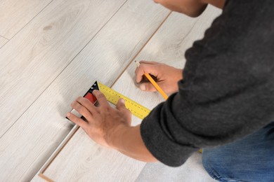 Photo of Professional worker using ruler during installationlaminate flooring, closeup