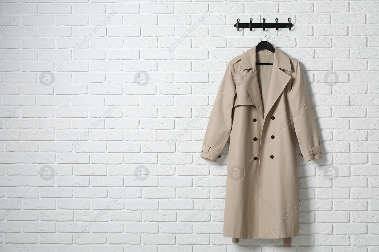 Photo of Hanger with beige coat on white brick wall, space for text