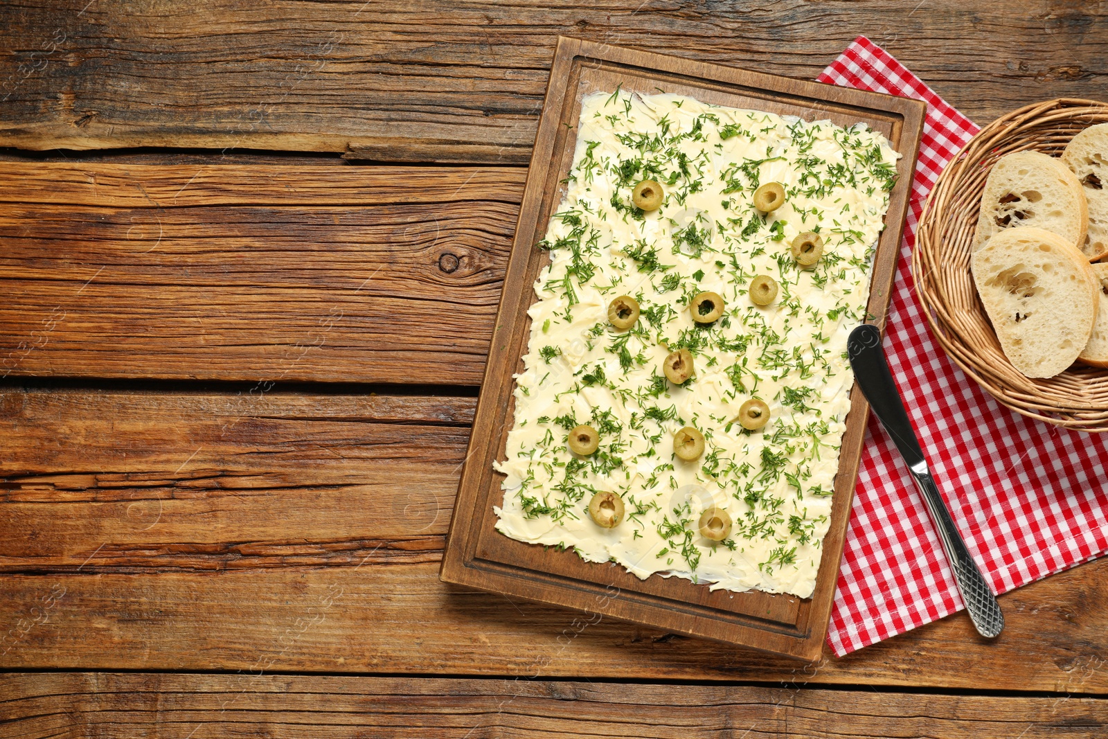 Photo of Fresh butter board with cut olives, bread and knife on wooden table, flat lay. Space for text