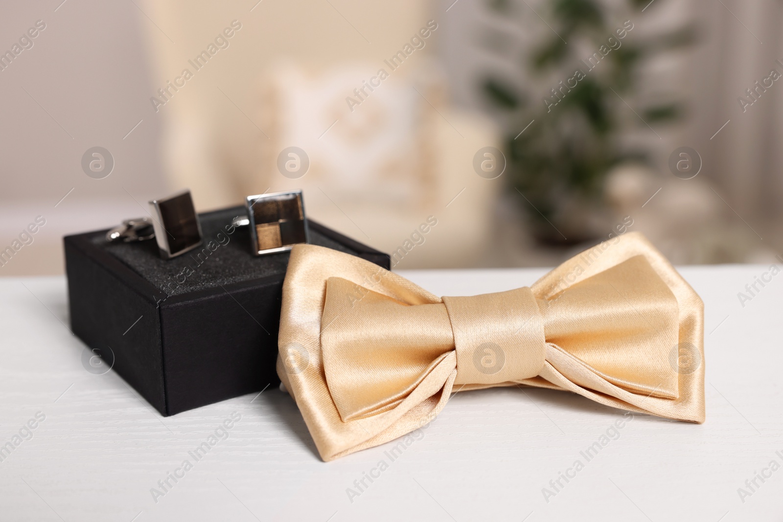 Photo of Stylish beige bow tie and box with cufflinks on white wooden table, closeup