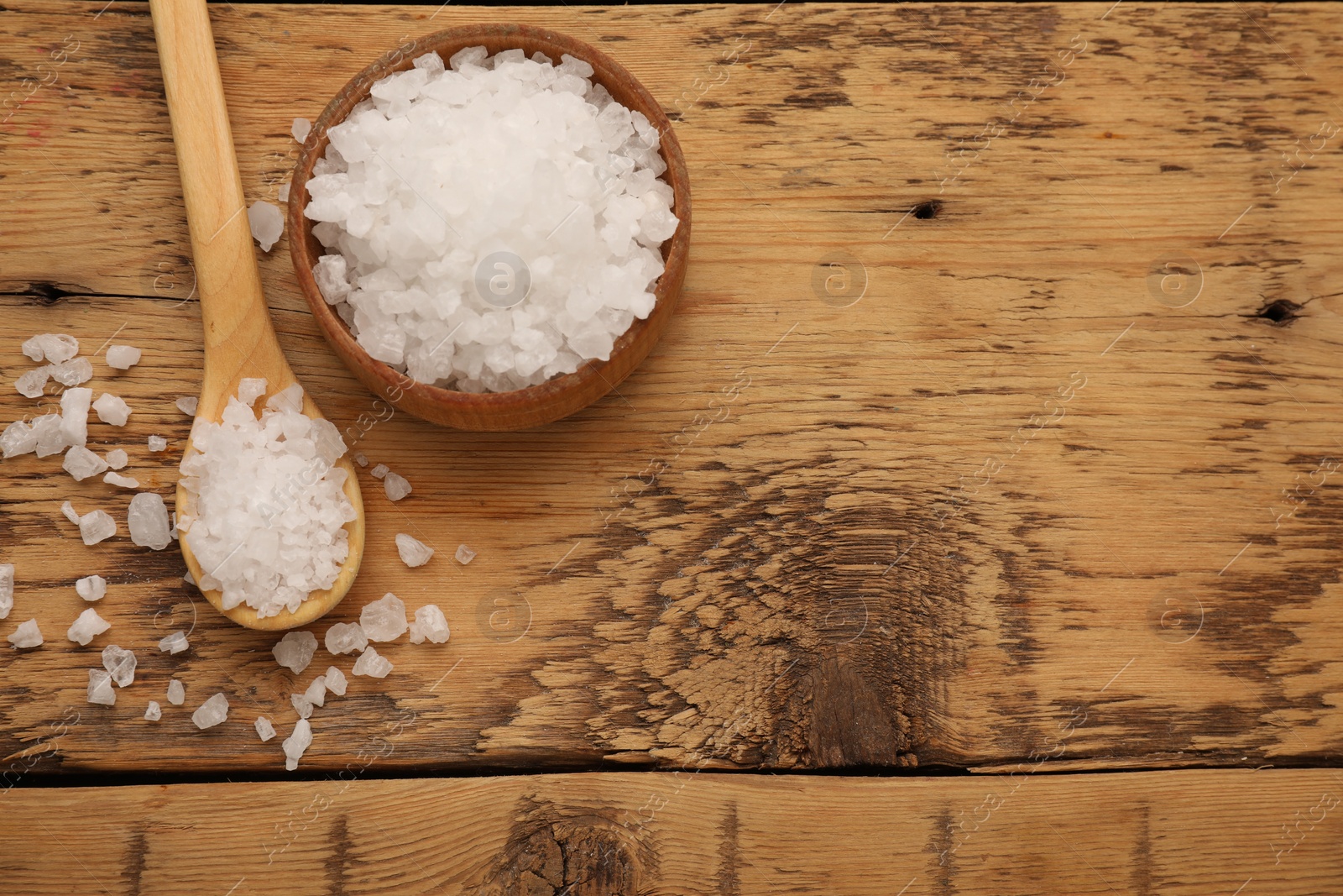 Photo of Bowl and spoon with sea salt on wooden table, flat lay. Space for text