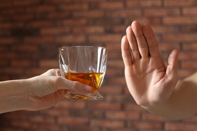 Man refusing to drink whiskey near red brick wall, closeup. Alcohol addiction treatment