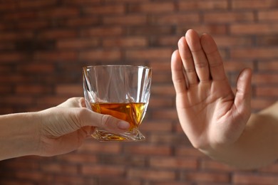 Photo of Man refusing to drink whiskey near red brick wall, closeup. Alcohol addiction treatment