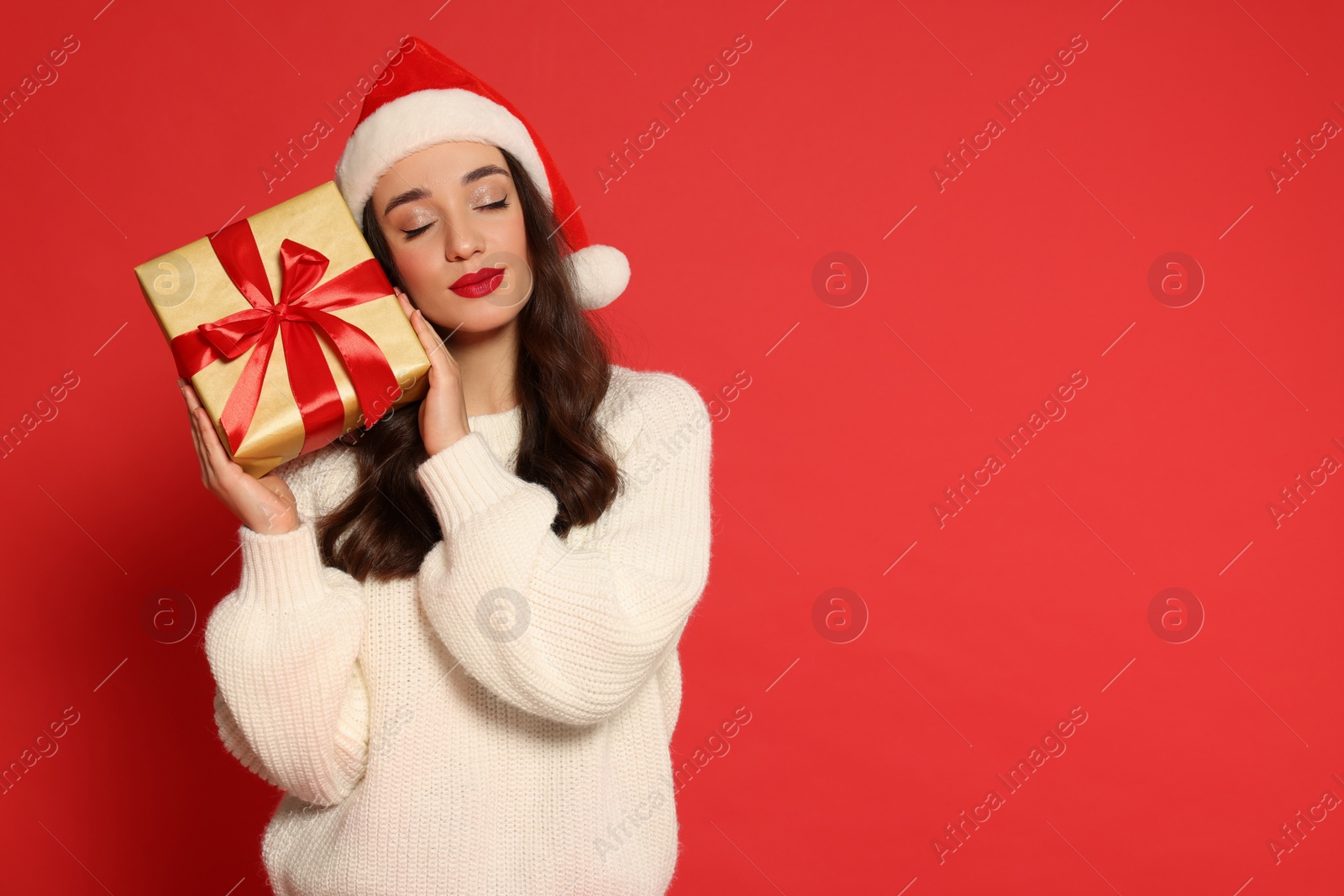 Photo of Beautiful young woman in Santa hat with Christmas gift on red background, space for text