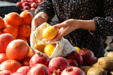 Woman putting lemon into cotton eco bag at wholesale market, closeup. Life without plastic