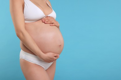 Photo of Pregnant woman in stylish comfortable underwear on light blue background, closeup. Space for text