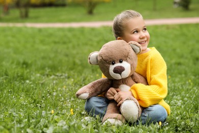 Little girl with teddy bear on green grass outdoors. Space for text