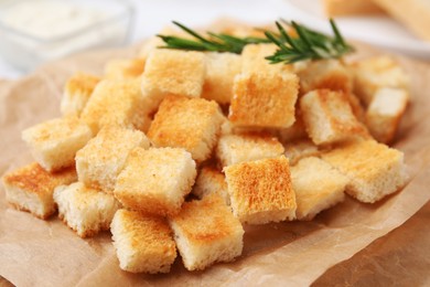 Photo of Delicious crispy croutons with rosemary on wooden board, closeup