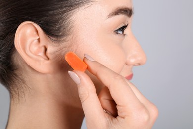 Photo of Young woman inserting foam ear plug on grey background, closeup