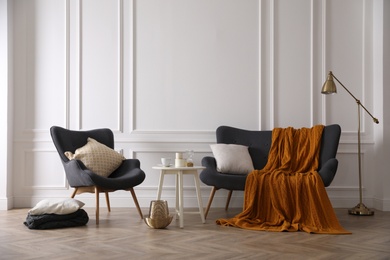 Photo of Comfortable sofa with knitted blanket, armchair and lamp in stylish room interior