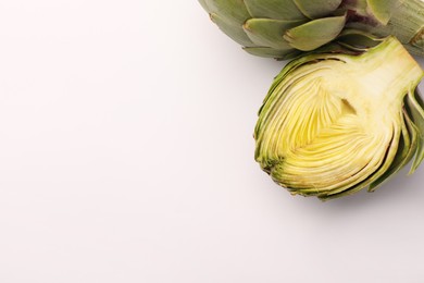Cut and whole fresh artichokes on white background, top view