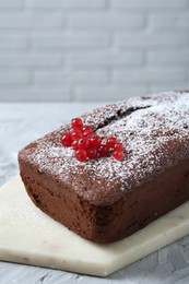 Photo of Tasty chocolate sponge cake with powdered sugar and currant on light grey textured table, closeup