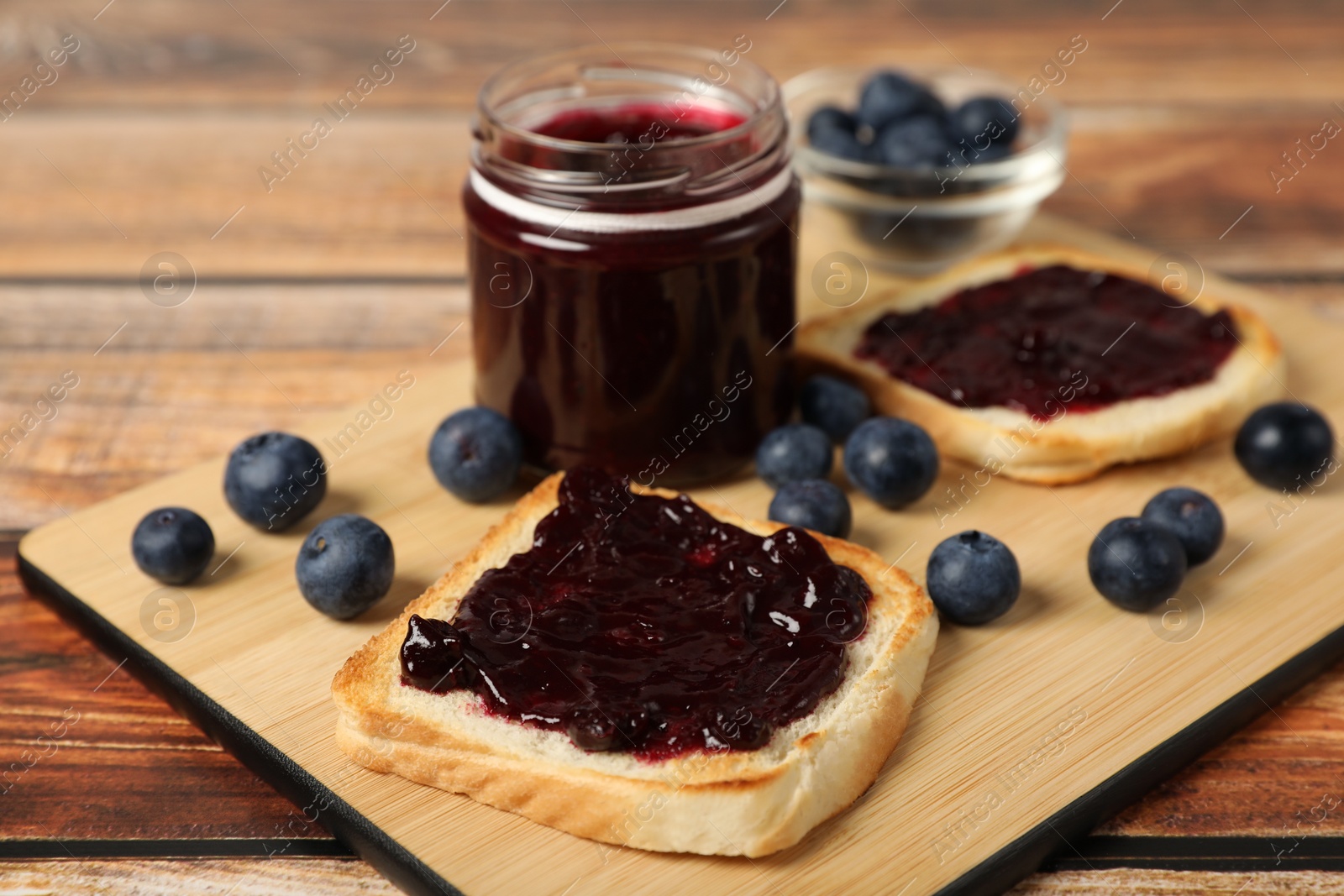 Photo of Delicious toasts with blueberry jam and fresh berries on wooden table